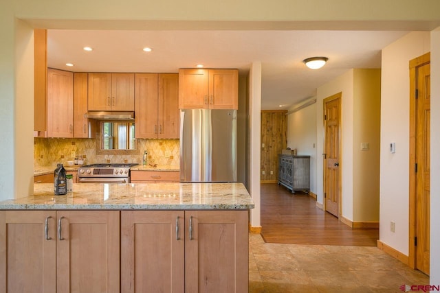 kitchen with kitchen peninsula, stainless steel appliances, decorative backsplash, light brown cabinetry, and light stone counters