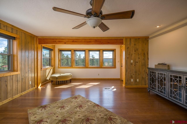 unfurnished room featuring ceiling fan, dark hardwood / wood-style flooring, wood walls, and a textured ceiling