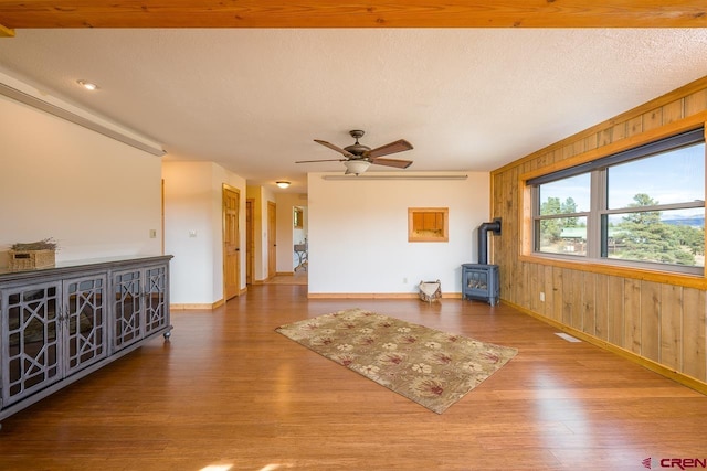 unfurnished living room with ceiling fan, wood-type flooring, wooden walls, a wood stove, and a textured ceiling