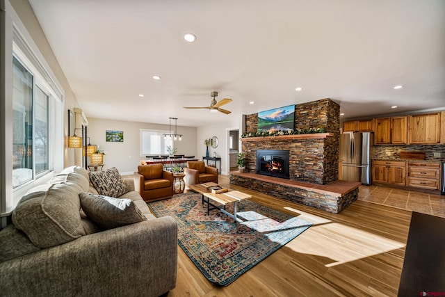 living room with ceiling fan, a stone fireplace, and light hardwood / wood-style flooring