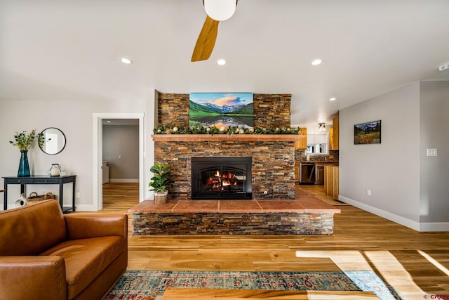 living room with ceiling fan, wood-type flooring, and a stone fireplace