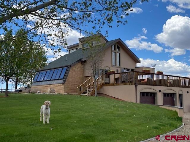 rear view of property with a lawn, a deck, and a garage