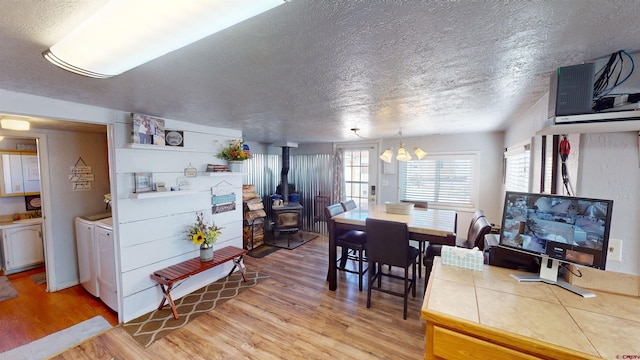 dining space with a textured ceiling, a wood stove, washing machine and clothes dryer, and light hardwood / wood-style flooring