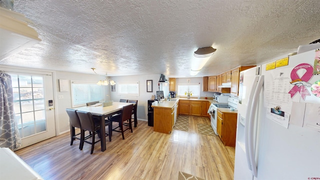 kitchen featuring kitchen peninsula, white appliances, pendant lighting, light hardwood / wood-style flooring, and a center island