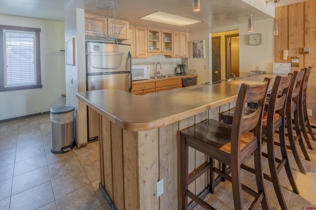 kitchen featuring sink, hanging light fixtures, kitchen peninsula, stainless steel refrigerator, and a breakfast bar area