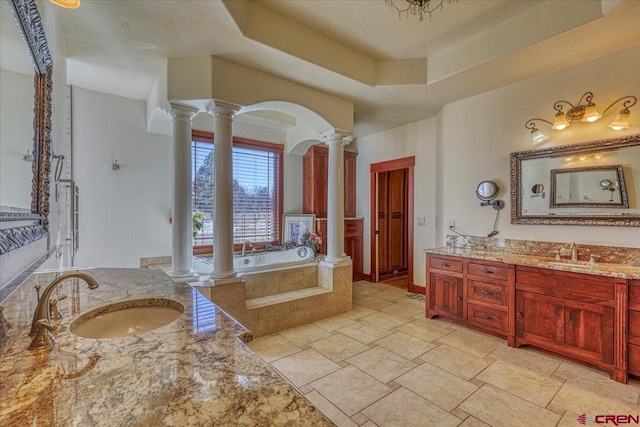 bathroom featuring tiled bath, ornate columns, a raised ceiling, and vanity