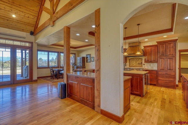 kitchen featuring premium range hood, light hardwood / wood-style floors, lofted ceiling, hanging light fixtures, and sink