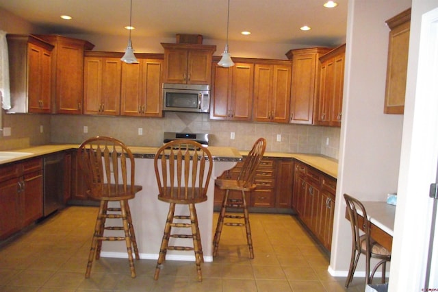 kitchen featuring pendant lighting, range, tasteful backsplash, light tile patterned flooring, and a breakfast bar