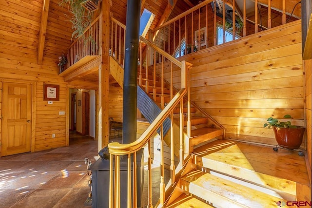 stairs with wood walls, beamed ceiling, high vaulted ceiling, and wooden ceiling