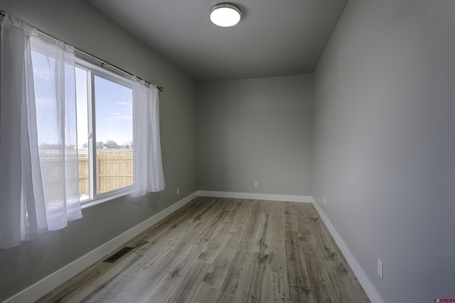 empty room with visible vents, light wood-style flooring, and baseboards