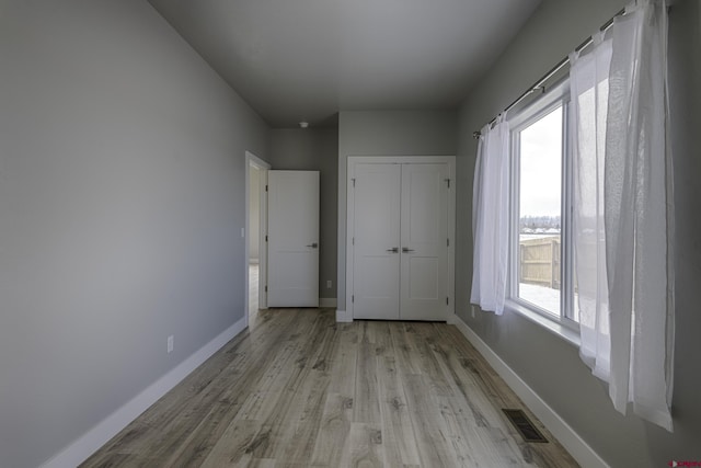 unfurnished bedroom with light wood-style floors, baseboards, visible vents, and a closet