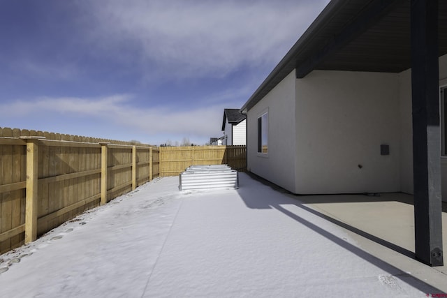 yard layered in snow with a fenced backyard and a patio