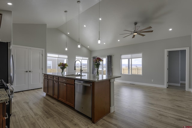 kitchen with stainless steel appliances, an island with sink, a sink, and light stone countertops