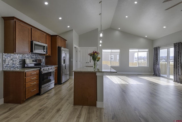 kitchen featuring a center island with sink, brown cabinetry, appliances with stainless steel finishes, light stone counters, and light wood-type flooring