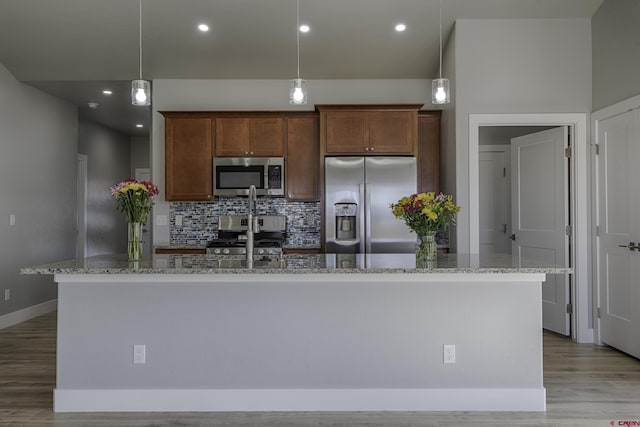 kitchen featuring stainless steel appliances, light stone counters, an island with sink, and pendant lighting