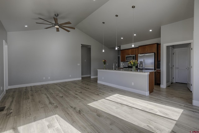 kitchen with open floor plan, appliances with stainless steel finishes, an island with sink, and pendant lighting