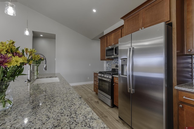 kitchen with a sink, vaulted ceiling, appliances with stainless steel finishes, light stone countertops, and pendant lighting