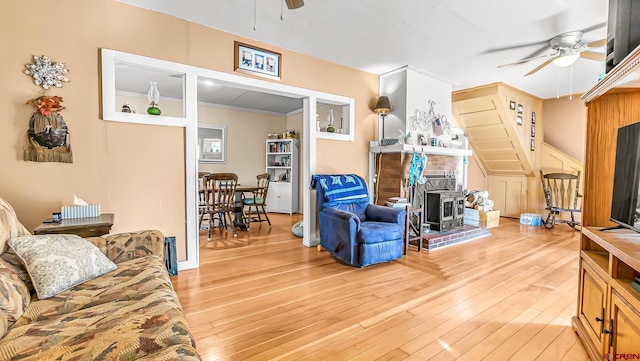 living room with ceiling fan, ornamental molding, light hardwood / wood-style floors, and a wood stove