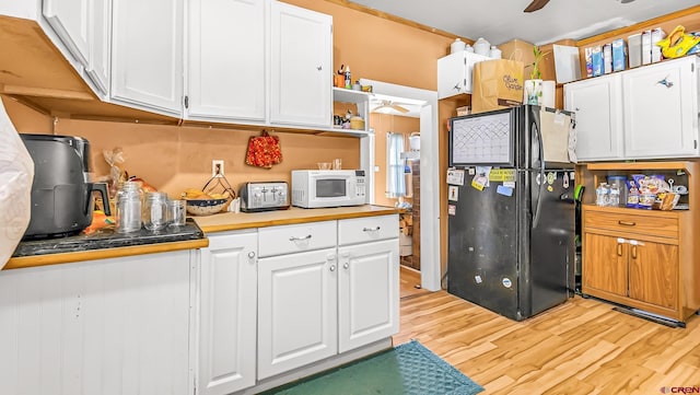 kitchen with ceiling fan, black refrigerator, white cabinetry, and light wood-type flooring