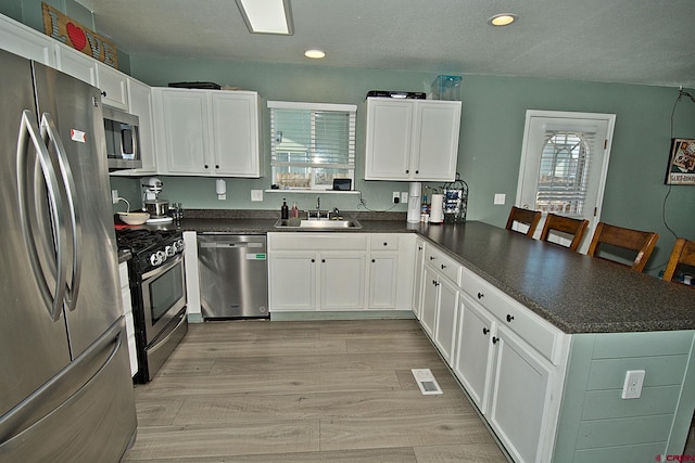 kitchen with white cabinets, kitchen peninsula, appliances with stainless steel finishes, and sink