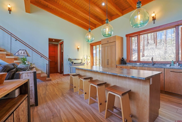 kitchen with wood ceiling, a kitchen bar, hanging light fixtures, light hardwood / wood-style flooring, and beamed ceiling