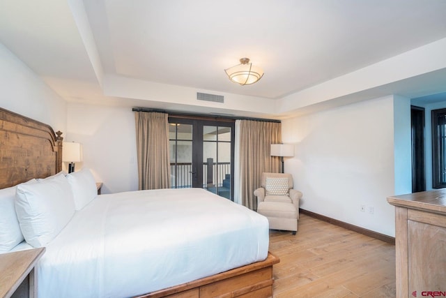 bedroom featuring light hardwood / wood-style flooring, a tray ceiling, and access to outside