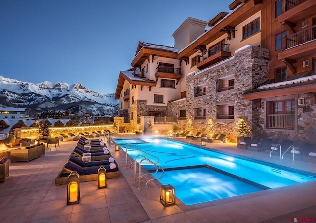 snow covered pool with a mountain view, a patio, and a hot tub