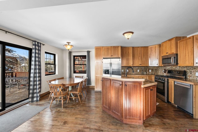 kitchen with a kitchen island with sink, sink, dark wood-type flooring, backsplash, and stainless steel appliances