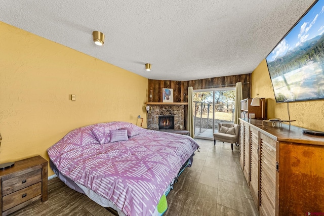 bedroom with a textured ceiling, access to exterior, wooden walls, and a fireplace