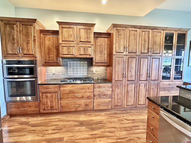 kitchen featuring light hardwood / wood-style floors, tasteful backsplash, dark stone counters, and stainless steel appliances