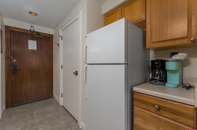 kitchen with a textured ceiling, light tile patterned floors, and white refrigerator