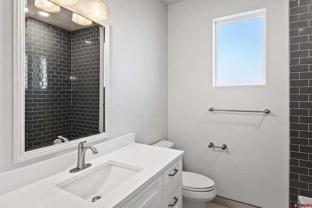 bathroom with a tile shower, toilet, and vanity