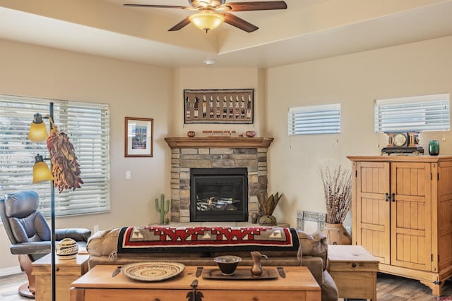 living room with hardwood / wood-style flooring, a raised ceiling, a stone fireplace, and ceiling fan