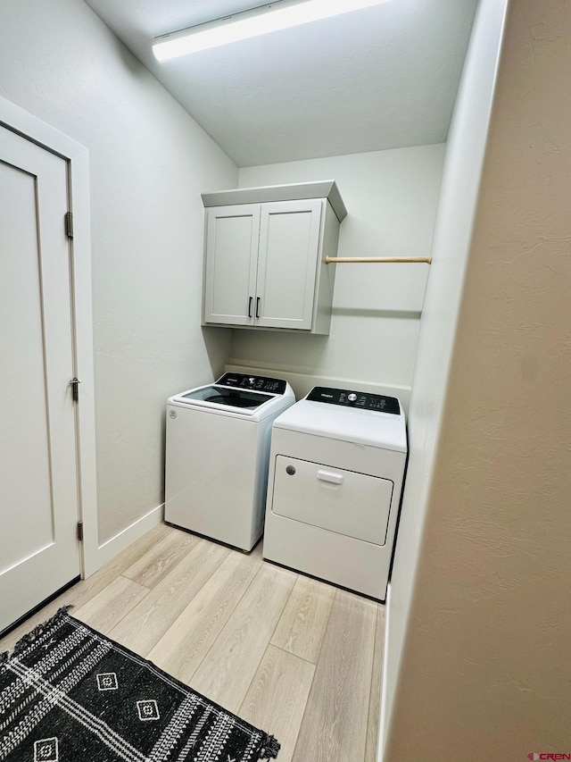 laundry area with washing machine and clothes dryer, light hardwood / wood-style floors, and cabinets