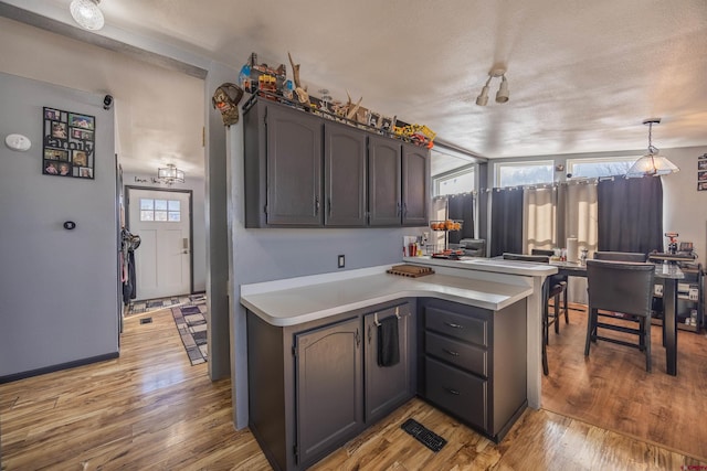 kitchen with dark brown cabinetry, decorative light fixtures, light hardwood / wood-style flooring, and a healthy amount of sunlight