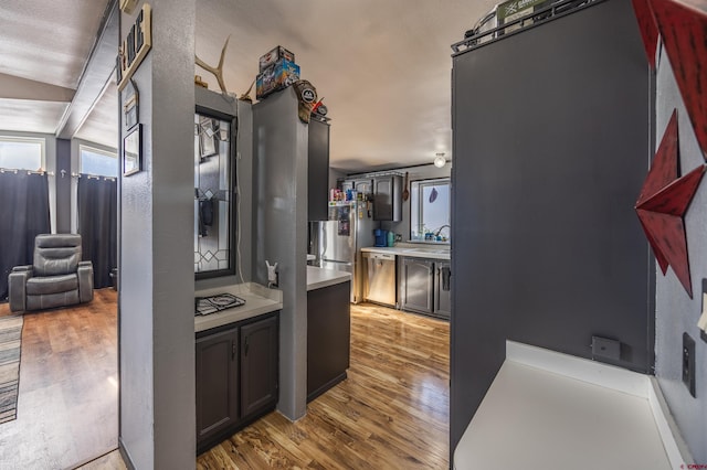 kitchen featuring appliances with stainless steel finishes, water heater, lofted ceiling, sink, and light wood-type flooring