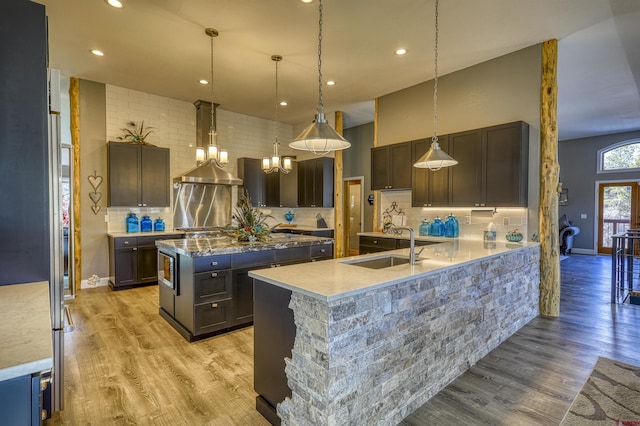 kitchen with decorative light fixtures, sink, a kitchen island with sink, dark brown cabinetry, and light hardwood / wood-style flooring