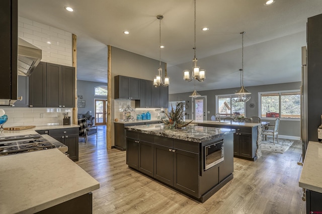 kitchen with built in microwave, a kitchen island with sink, decorative backsplash, and decorative light fixtures