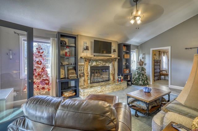 living room featuring lofted ceiling, a stone fireplace, and ceiling fan