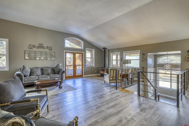 living room featuring french doors, vaulted ceiling, light hardwood / wood-style floors, and a wood stove