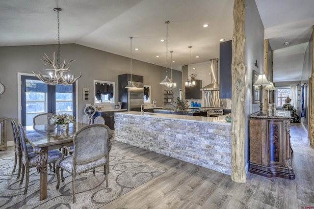 kitchen featuring pendant lighting, an island with sink, lofted ceiling, hardwood / wood-style flooring, and an inviting chandelier