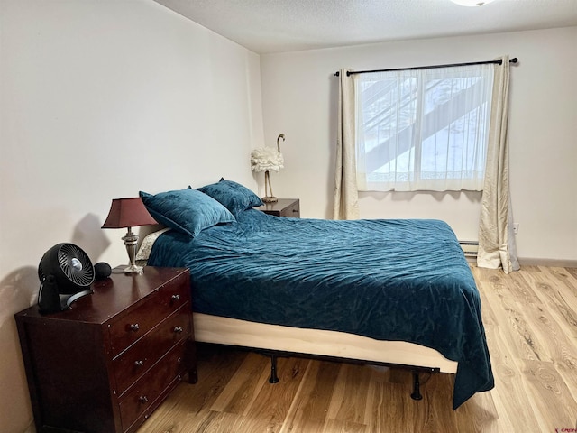 bedroom featuring a baseboard radiator, light hardwood / wood-style floors, and a textured ceiling