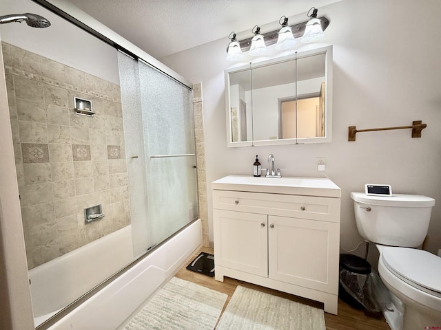 full bathroom with hardwood / wood-style flooring, shower / bath combination with glass door, vanity, a textured ceiling, and toilet