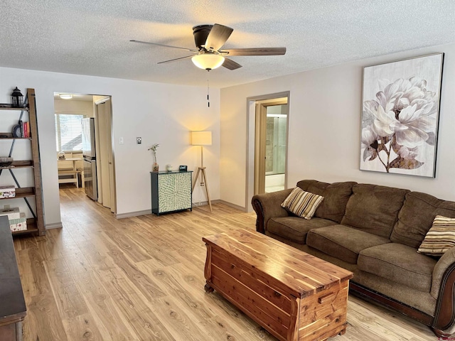 living room with a textured ceiling, ceiling fan, and light wood-type flooring