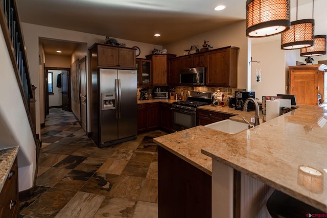 kitchen featuring decorative light fixtures, sink, kitchen peninsula, stainless steel appliances, and light stone countertops