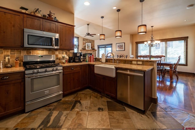 kitchen with lofted ceiling, sink, appliances with stainless steel finishes, decorative light fixtures, and kitchen peninsula