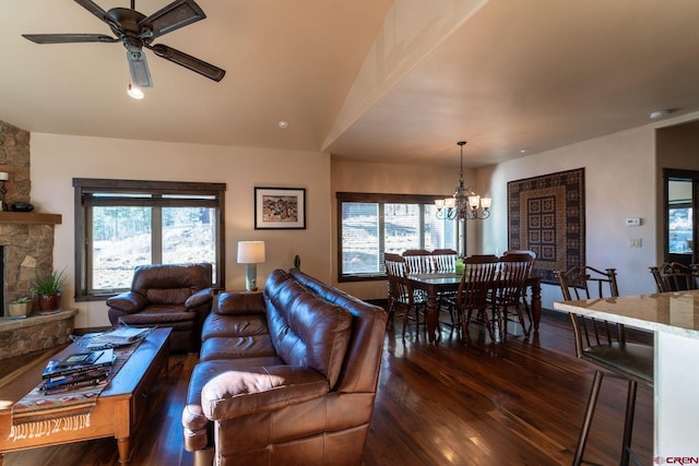 living room featuring vaulted ceiling, a stone fireplace, dark hardwood / wood-style floors, and ceiling fan with notable chandelier