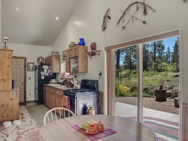 kitchen featuring black fridge, high vaulted ceiling, and gas range oven