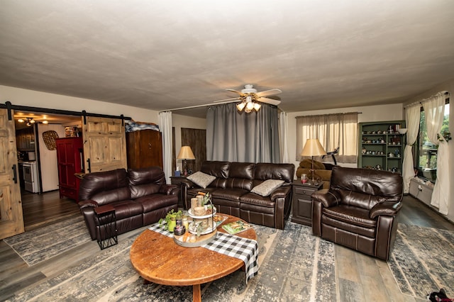 living room with ceiling fan, a barn door, and dark hardwood / wood-style flooring