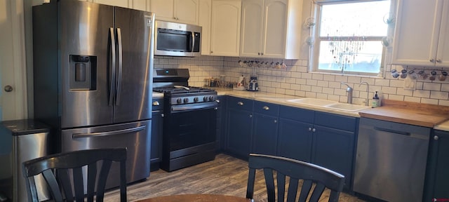 kitchen with appliances with stainless steel finishes, blue cabinets, sink, white cabinets, and backsplash